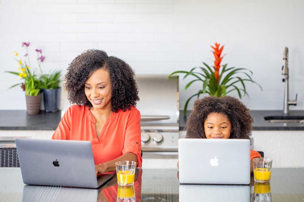 A mother and daughter sitting at a kitchen island, both on their laptops messaging