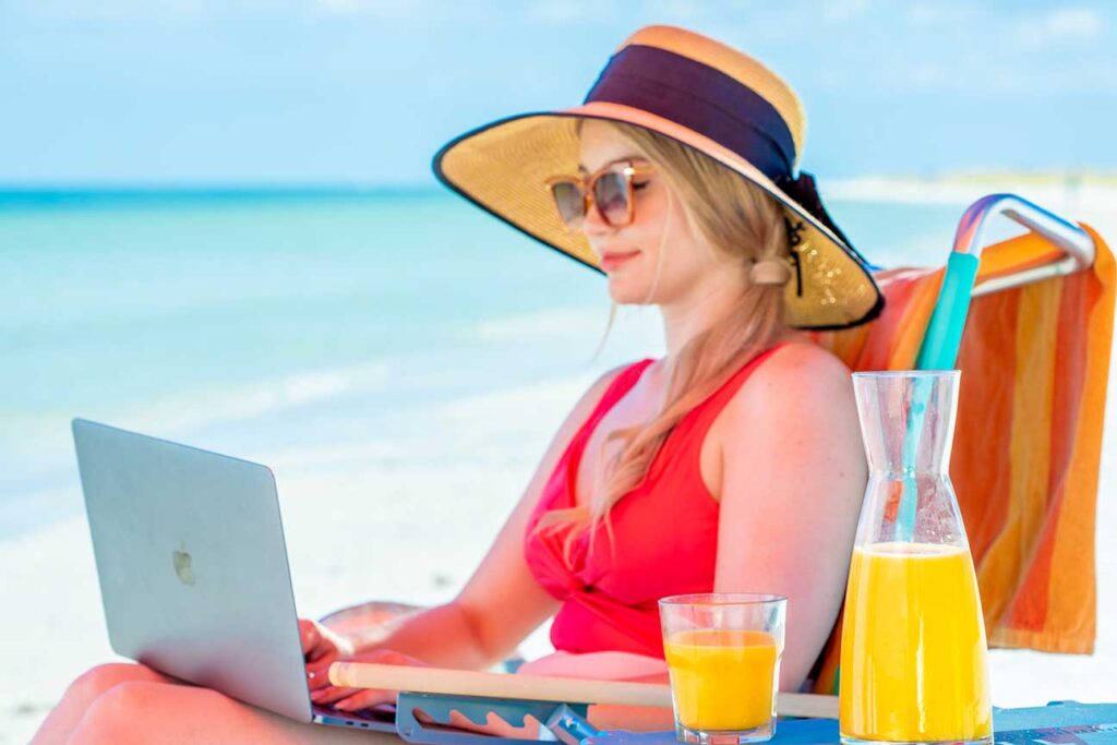 A woman reading the news on her laptop by the beach with a glass of Florida Orange Juice