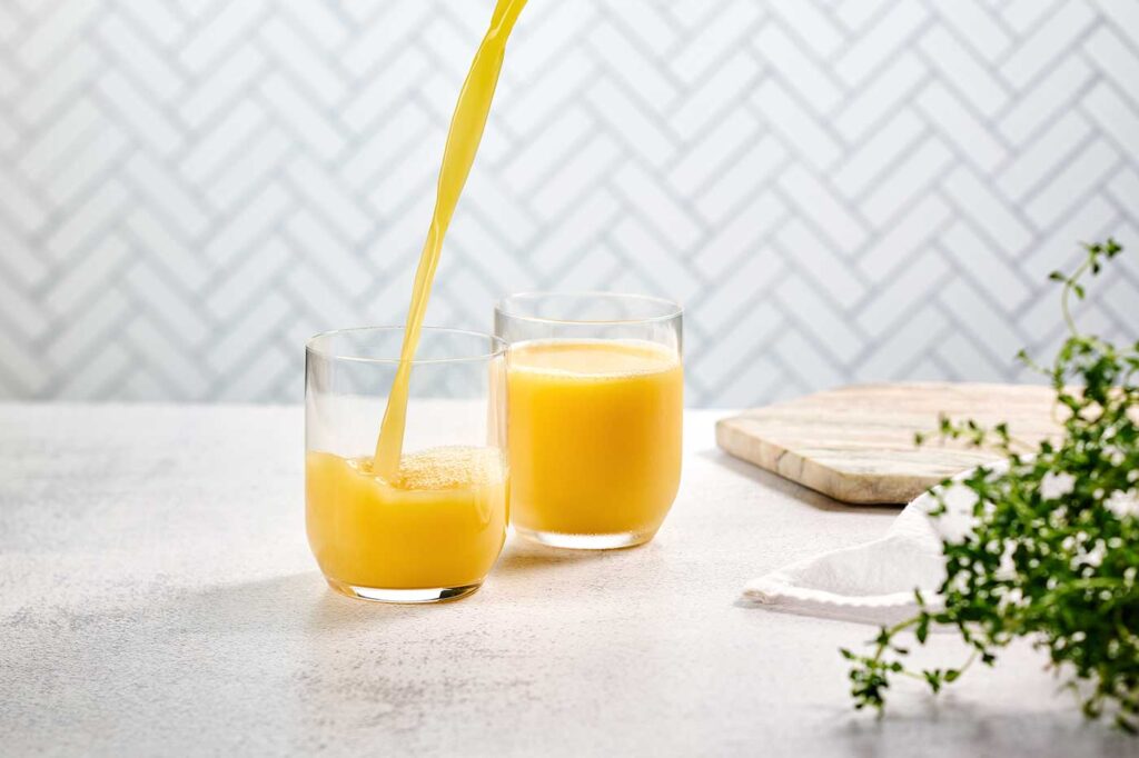 Two glasses of Florida Orange Juice with fresh OJ being poured into one