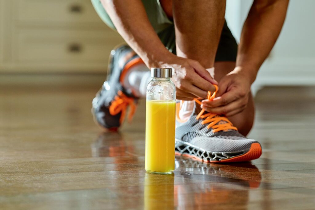 A person tying their running shoe, next to a glass of orange juice, before a jog