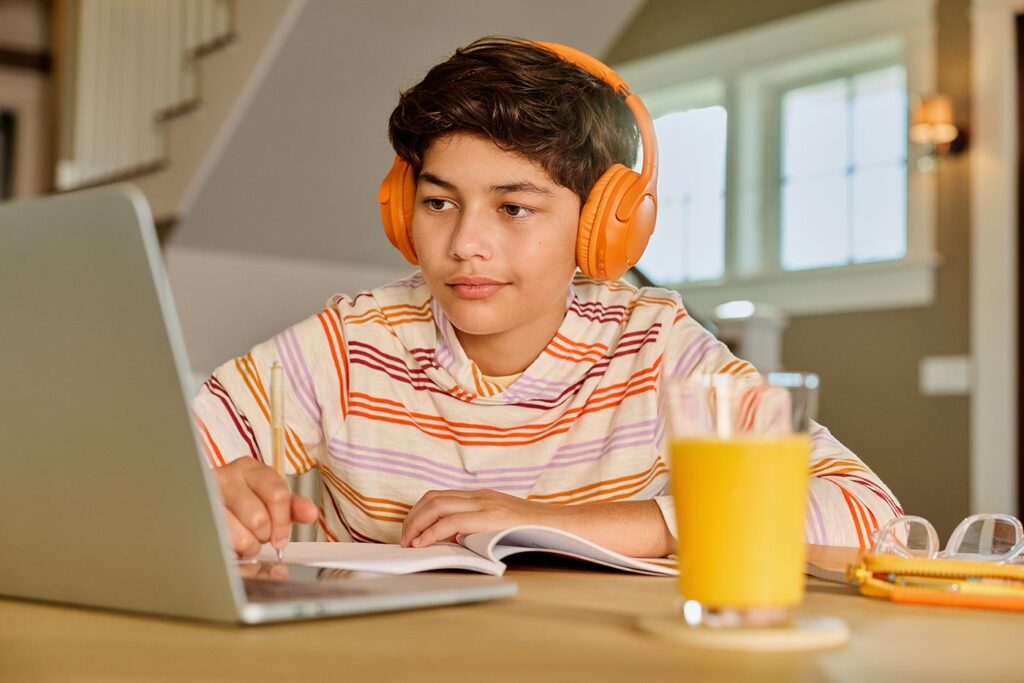A kid wearing orange headphones doing homework with a glass or Florida Orange Juice