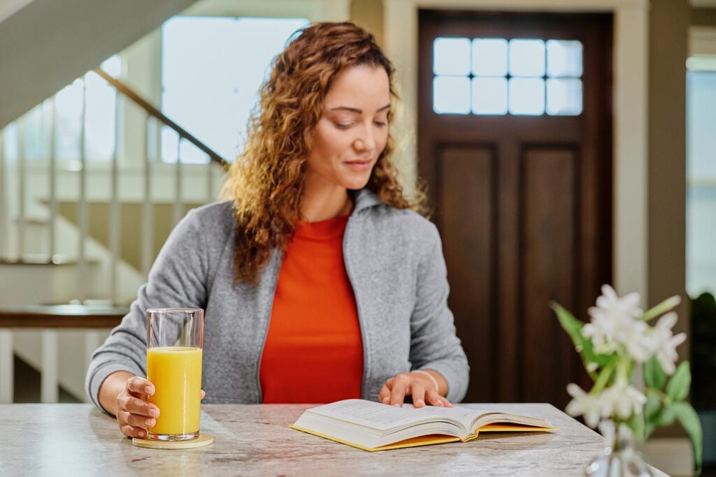 A woman reading a book with a class of Florida Orange Juice