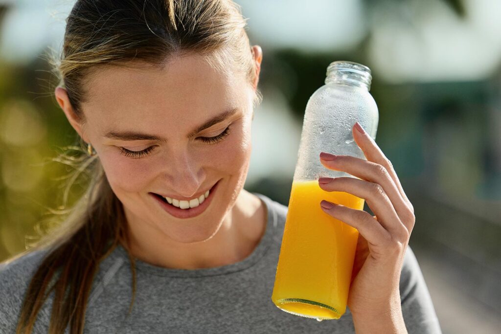A woman outside in the sun on a nice day with a bottle of orange juice