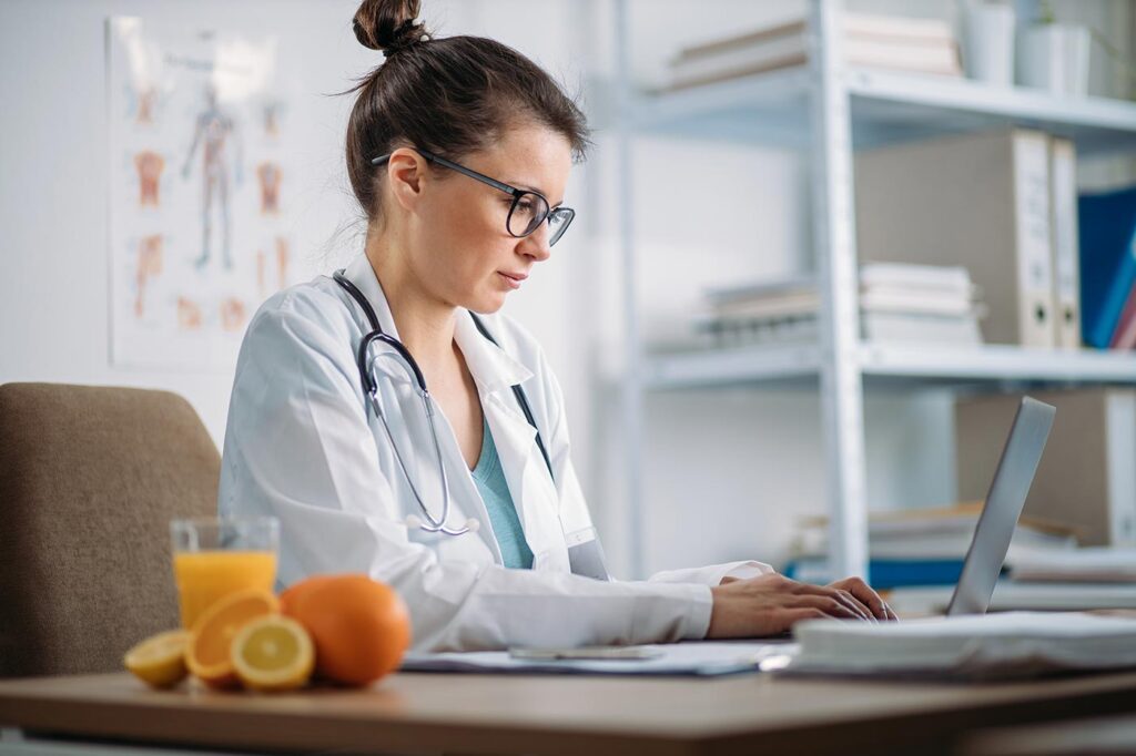 Doctor in her office typing on her laptop with fresh Florida Oranges on her desk