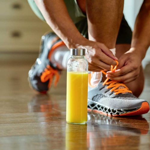 A person tying their running shoe, next to a glass of orange juice, before a jog